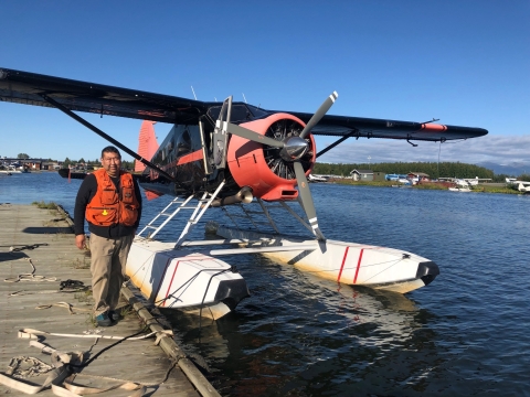 A pilot stands on a dock with a large single engine plane on floats 