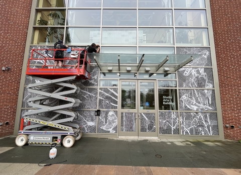 Two people on a construction lift apply decals to the front of a building