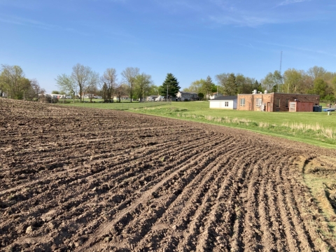 Unplanted sloped farm field next to two buildings with grass between them. 