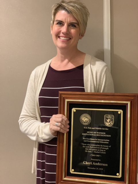 A woman smiles while holding up an award
