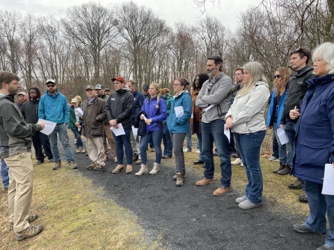 A large group of people gather in front of a person talking outside