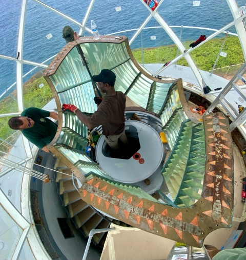 An overhead of people inside of a lighthouse taking down the lens. 