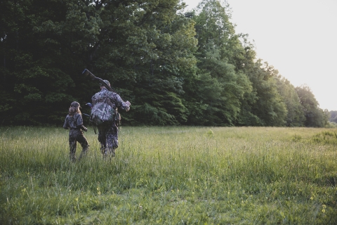Adult and child in camouflage walk into New England woods. 