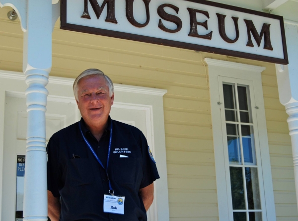 A smiling volunteer stands under the museum sign on the front porch of the National Fisheries Museum building.