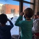 Children use binoculars at a window