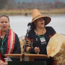 Two native singers, with one wearing a straw hat and holding a drum, behind a podium