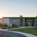he left side of a brick-and-mortar buidling is illuminated by the sunrise peeping above the treeline.