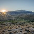 A sagebrush landscape at sunrise. A fence runs through the foreground and there are mountains stretching into the distance.