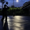 Two people standing in a river at night, looking up at a bridge