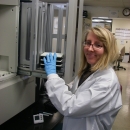 A molecular geneticist in a conservation genetics laboratory wearing a lab coat poses with some samples near some equipment.