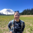 Hannah Ferwerda standing in a field with Mount Rainier in the background with trees and blue sky.