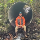 Andy Stevens sitting at the end of a culvert with water running through it.