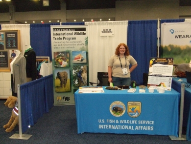 A woman stands behind a table with a tablecloth that reads U.S. Fish and Wildlife Service International Affairs