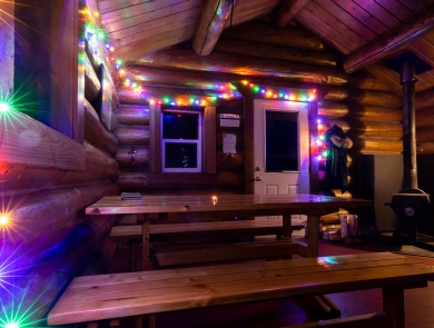 Colored lights decorate the cozy interior of the Dolly Varden log public use cabin at Kenai Refuge on Dolly Varden Lake.