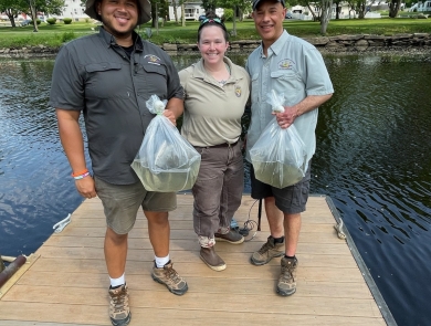 Three people holding fish on a pier above a river.