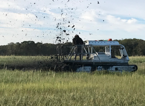 FWS staff using what looks like an atv with tank treads to cut through the marsh and carve the earth to create runnels.