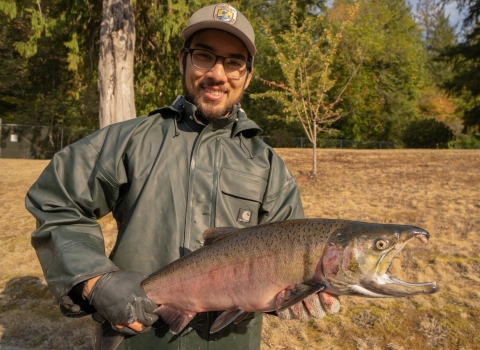 Intern Eric Klingberg poses holding a adult coho salmon at the Quilcene National Fish Hatchery in Quilcene Washington.