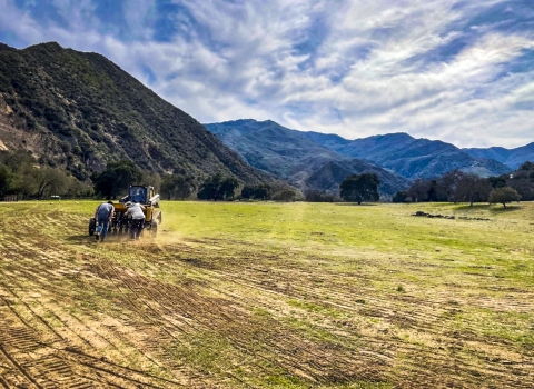 A drill seeder being pushed along a wide open field
