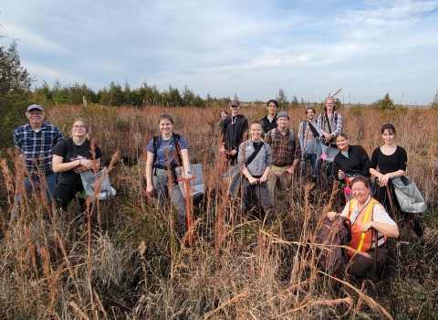 A group of people stand smiling in tallgrass outside