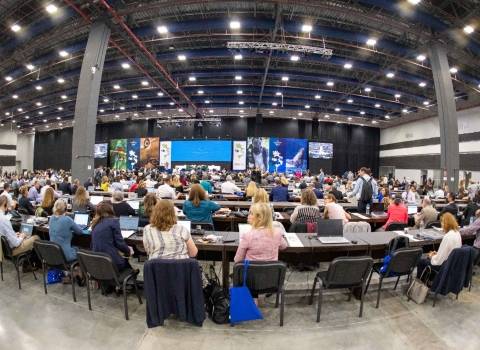 A large meeting space with people sitting at long tables