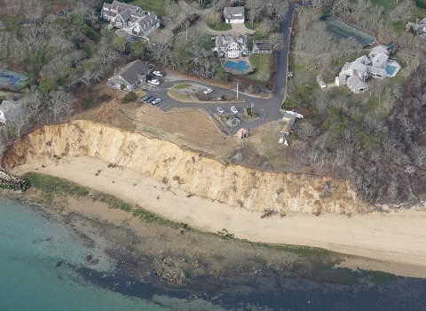 an aerial view of an eroding coastal bluff on a national wildlife refuge property. Buildings, a parking lot and trees can be seen surrounding the property