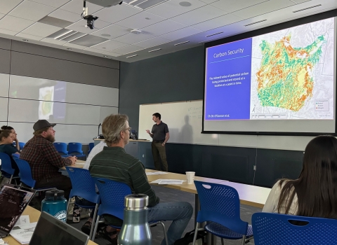 presentor in classroom of students with map on screen