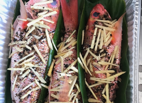 Three red fish in leaves are seasoned for cooking