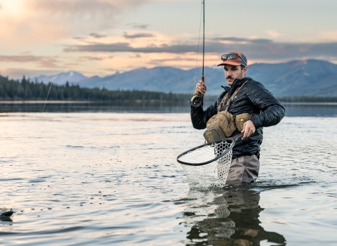 Man holds fly rod and net as he catches a trout. 