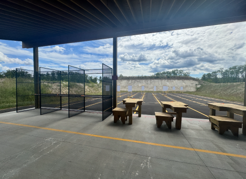 Empty firing line shows updated wooden shooting benches and range berm in the background