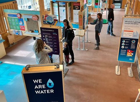 From a birds eye view, panels and exhibit pieces are places throughout a large open building. People are milling about. 