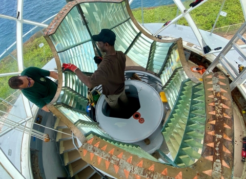 An overhead of people inside of a lighthouse taking down the lens. 