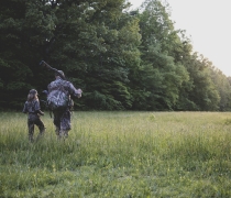 Adult and child in camouflage walk into New England woods. 
