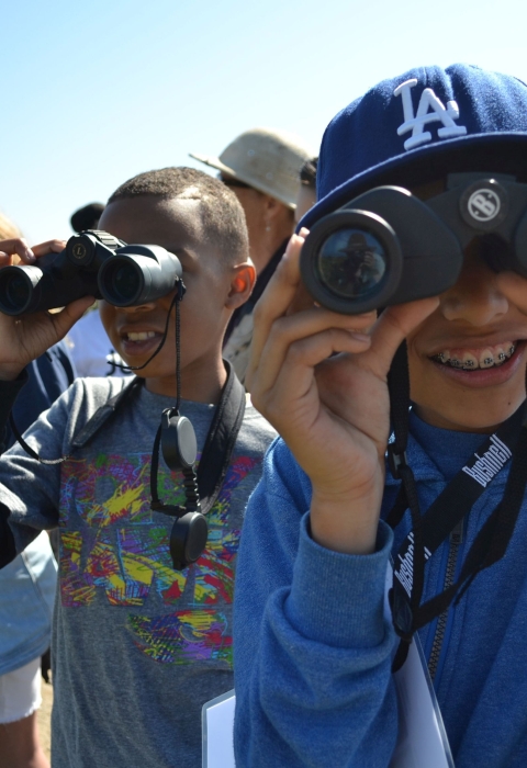 Smiling youngsters use binoculars to look at birds at San Diego Bay National Wildlife Refuge.