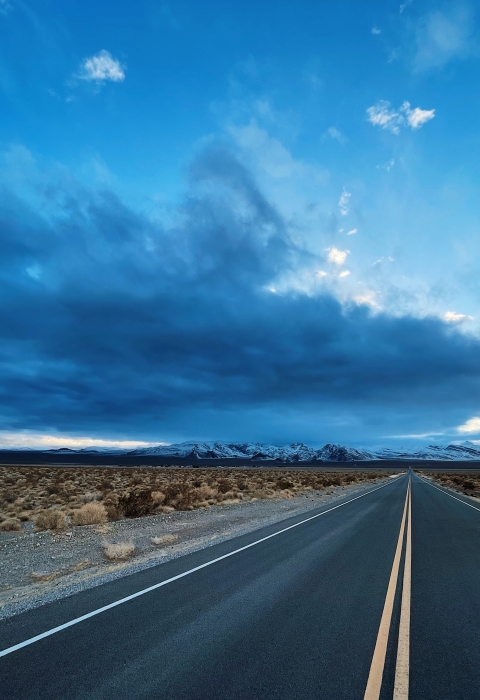 An empty road heads into the distance while dark, ominous clouds fill the sky above