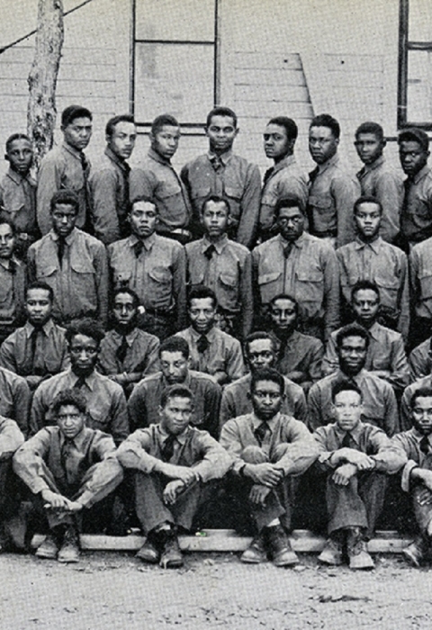 Black and white photo of more than 100 young African American men in uniform posing in front of a building