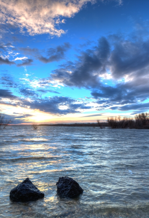 Sun just below horizon over lake with dramatic clouds above.