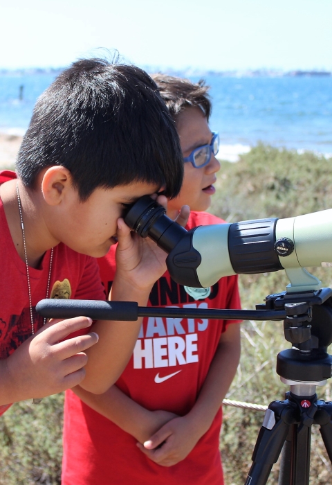 Two young boys use a spotting scope 