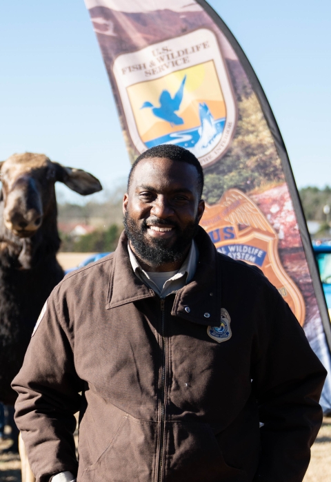 A man in a brown uniform stands in front of a FWS banner