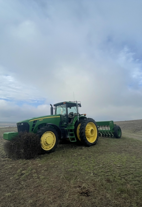 A tractor is in the middle of the frame with bare ground and a cloudy sky 