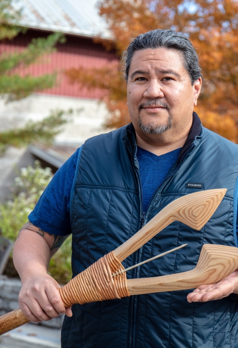 up close image of man holding wooden spear with fall leaves in background