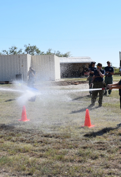 2 groups of people face ech other holding fire hoses whose spray hits the other