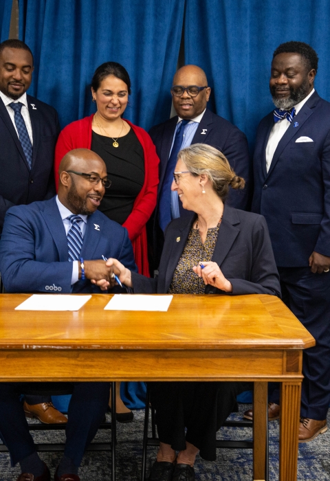6 dressed up people behind 2 at table shaking hands
