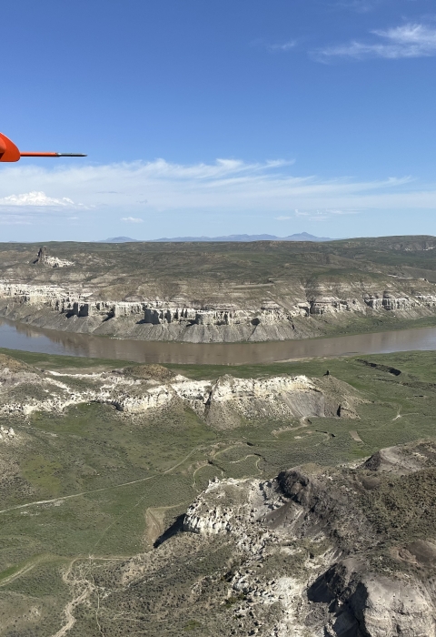 view of an airplane wing over the landscape of a river 