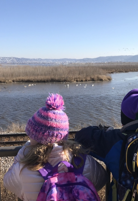 Students in winter gear stand in front of a railing over looking the Mississippi River