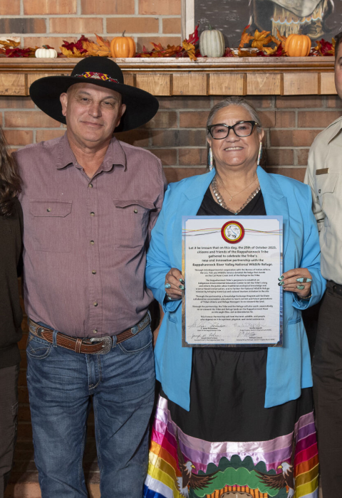 Four people stand together smiling as a woman in blue holds a signed document