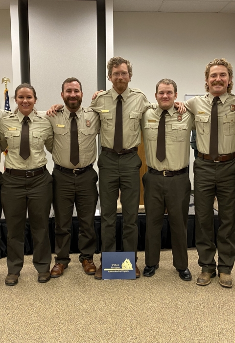 Seven recent graduates of the wildland fire apprentice program pose for a photo in their uniforms