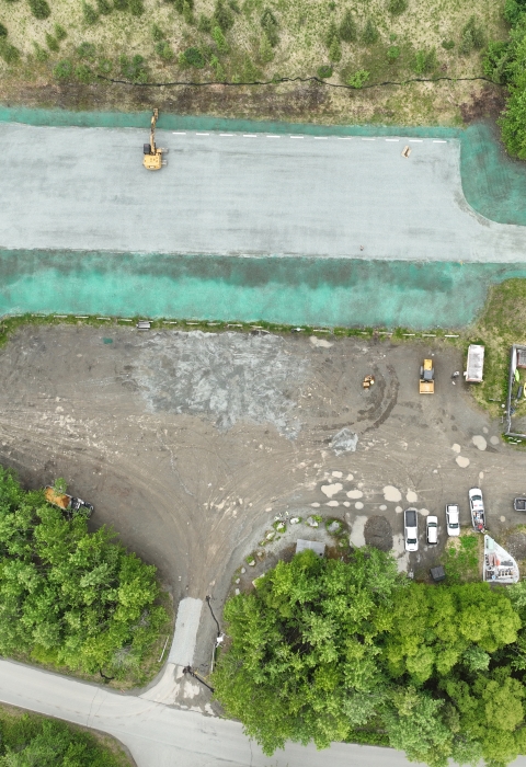 Aerial view of a parking lot with tall woodland surrounding it.