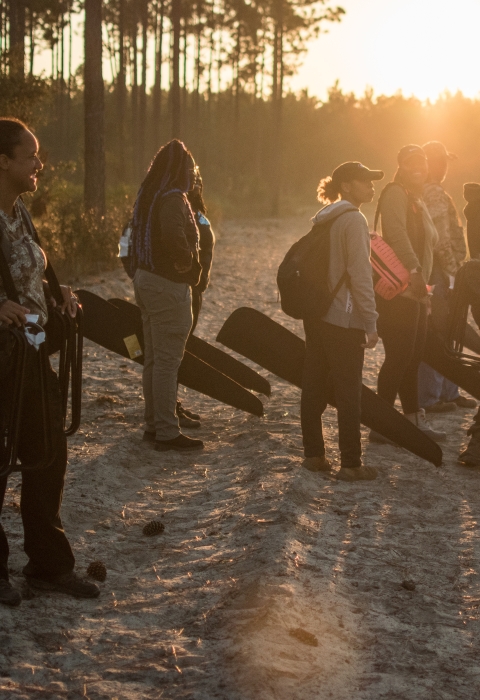 Fort Valley State University students, dressed for hunting, stand on dirt road at sunrise.