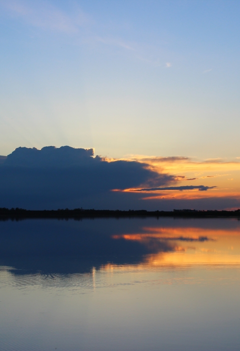 Silhouette of a man fishing as the sun sets over the water.