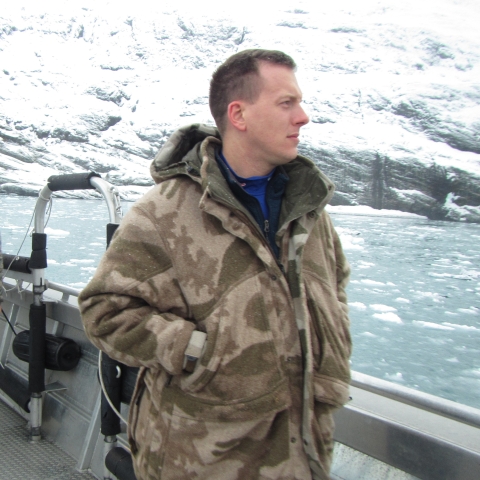 Man dressed in camouflage on a boat surrounded by a glacier